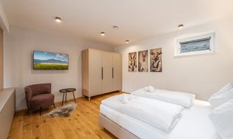 A modern bedroom with a double bed, a television, and a cozy sitting area. The walls are decorated with artistic pictures.