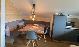 A modern furnished dining area with a wooden stove table and comfortable chairs. The walls are clad in wood and a pleasant lighting creates a relaxed atmosphere.