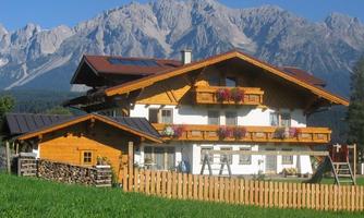 A charming alpine house with wooden cladding and colorful flower balconies. In the background, a majestic mountain landscape rises.