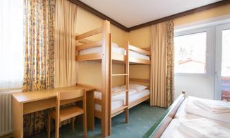 A bright room with a bunk bed and a desk. The windows are decorated with curtains and the carpet has a green hue.