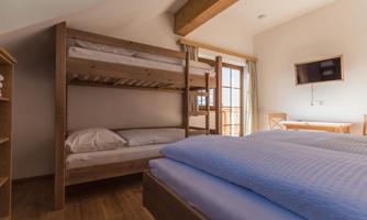 A cozy bedroom with a double bed and a bunk bed. Large windows provide plenty of daylight.