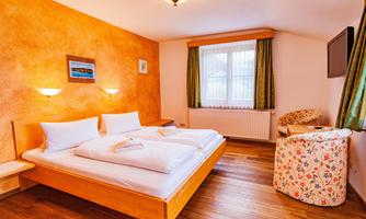 A cozy bedroom with a double bed and wooden floor. The walls are painted in warm colors and there is a comfortable armchair in the corner.