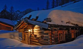 A charming wooden cabin, covered in snow, stands in a wintry landscape. The gentle glow of a light illuminates the cabin at twilight.
