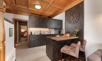 A modern kitchen with a wooden ceiling and elegant dark cabinets. The dining area is furnished with two chairs and a small wooden table.