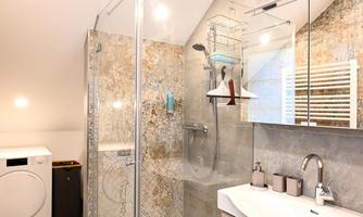 A modern bathroom with a glass shower and a spacious sink area. A laundry room is also available.