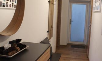 A bright hallway with wooden floors and modern furniture. Photos hang on the wall, and there is a mirror as well as a hook for hanging.