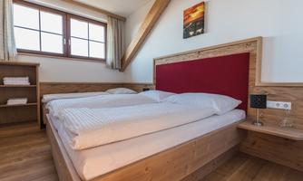 A cozy bedroom with a double bed and wood-colored furniture. The room has large windows and a warm, inviting hue.