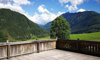 A beautiful view from a terrace of green hills and tall mountains. The sky is blue with some clouds.