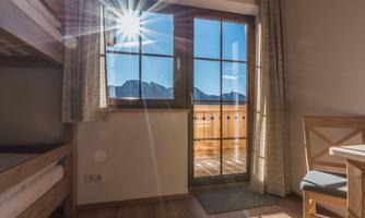 A bright room with a window that leads to a balcony with a mountain view. The sun shines through the window, creating a friendly atmosphere.