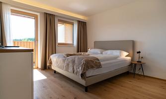 A modern bedroom with a large bed and bright curtains. The room has a balcony with an outdoor view.