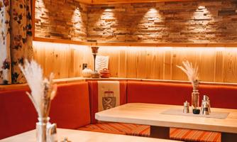 A cozy restaurant interior with wood paneling and warm lighting. The seating area is furnished with orange cushions and decorative elements.
