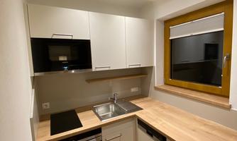 A modern, compact kitchen with bright cabinets and a wooden countertop. It includes a stove, sink, and microwave, as well as a window that lets in daylight.