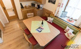 A cozy dining area with a large table and a bench. In the background, a kitchenette and decorative elements are visible.
