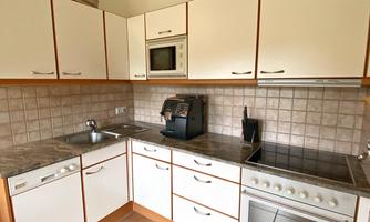 A modern kitchen with white cabinets and a stone countertop. The equipment includes a stove, an oven, and a coffee machine.