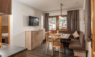 A cozy living room with a dining area and a modern kitchenette. Large windows provide plenty of daylight and offer a view outside.