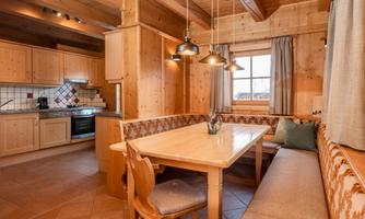 A cozy kitchen in alpine style with wooden paneling and a large dining area. The atmosphere is warm and inviting, ideal for shared meals.