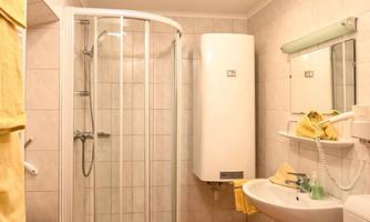 A modern bathroom with a shower cabin and a sink. Yellow towels and a small wooden cabinet give the room a warm atmosphere.