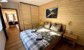 A cozy bedroom with a wooden wall design and a double bed. In the background, there is a door leading to another room.