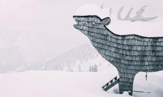 A wooden figure of a reindeer stands in the snow-covered landscape. The sky is gray and it looks wintry.