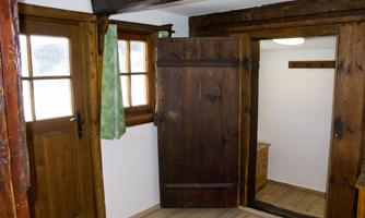 A room with rustic wood design and two doors. A vertical wooden door opens to another room.