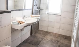 A modern bathroom with wood and stone tiles. There is a sink, a toilet, and a shower with plenty of light from the window.