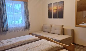 A cozy bedroom with two single beds and a light wood ceiling. A mirror and pictures of natural scenes hang on the wall.