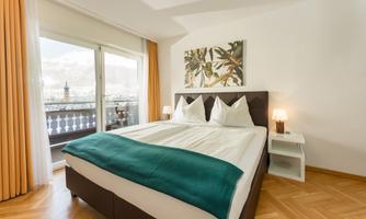 A modern bedroom with a double bed and a cozy carpet. Large windows offer a view of the mountains and let in a lot of light.