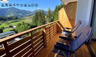 A cozy balcony with two chairs and a view of the mountains. The surroundings are green and inviting.