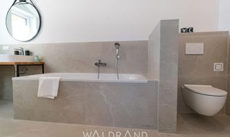 A modern bathroom with an elegant bathtub and a toilet.  
Large tiles and a round mirror give the space a clean, contemporary look.