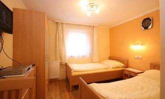 A simple bedroom with two beds and a window. The walls are painted orange, and there is a television as well as a clock on the wall.