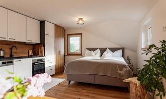 A modern bedroom with a cozy bed and a small kitchenette. Bright colors and natural materials give the room an inviting atmosphere.