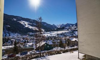 A snow-covered landscape with mountains in the background. The sun shines brightly over the picturesque village.