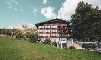 A charming hotel in the mountains with large windows and a beautiful garden. In the background, the majestic mountains are visible.