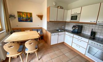 A modern kitchen with a small dining area. The walls are light, and the furniture is made of wood with an inviting design.