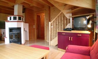 A cozy living space with wooden beams and a fireplace. A red sofa and a television complement the decor.