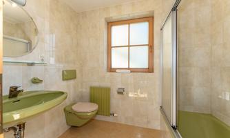A modern bathroom with green sanitary facilities and tiles. The window provides plenty of daylight.