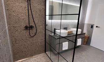 A modern bathroom with a walk-in shower and stylish tiles. The large mirrored wall reflects the elegant design.
