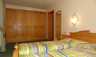 A simple bedroom with a wooden bed and striped bedspreads. The room has wooden closets and soft lighting.