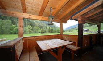 A cozy wooden terrace with a table and a bench. In the background, green meadows and mountains are visible.