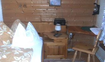 A cozy room with wooden paneling and a bed with decorative pillows. A small desk and a chair complete the space.