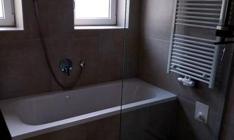 A modern bathroom with a bathtub and a large glass shower door. Two windows provide natural light and a welcoming space.