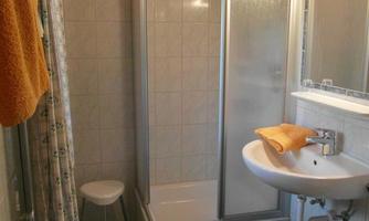 A modern bathroom with a shower, a sink, and a toilet. Towels and a small seating area complete the overall picture.
