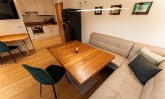 A modern living room with a wooden table and a comfortable couch. The kitchen is open and well-equipped.