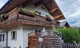 A cozy house with a beautiful wooden balcony and flowers. In the foreground, you can see a lovely fence and lots of greenery.