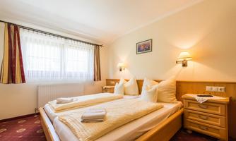 A cozy bedroom with two beds and warm wooden interiors. The room has large windows that let in plenty of daylight.