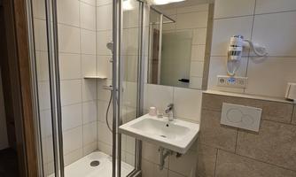 A modern bathroom with a shower cabin, a sink, and a toilet. The walls are brightly tiled, and there is a large mirror.