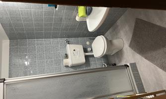 A modern bathroom with gray tiles. There is a shower, a toilet, and a sink with towels.