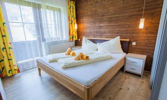 A cozy bedroom with a large bed and wooden paneling. Bright curtains and a modern bedside lamp create an inviting atmosphere.