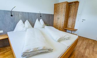 A modern bedroom with a double bed and two white bed covers. There is a wooden wardrobe and a pleasant, simple decor.