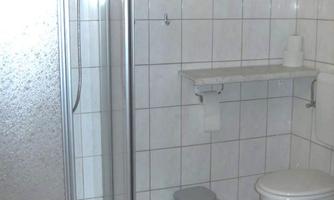 A simple bathroom with a shower, a toilet, and a small shelf. The walls and floor are tiled.